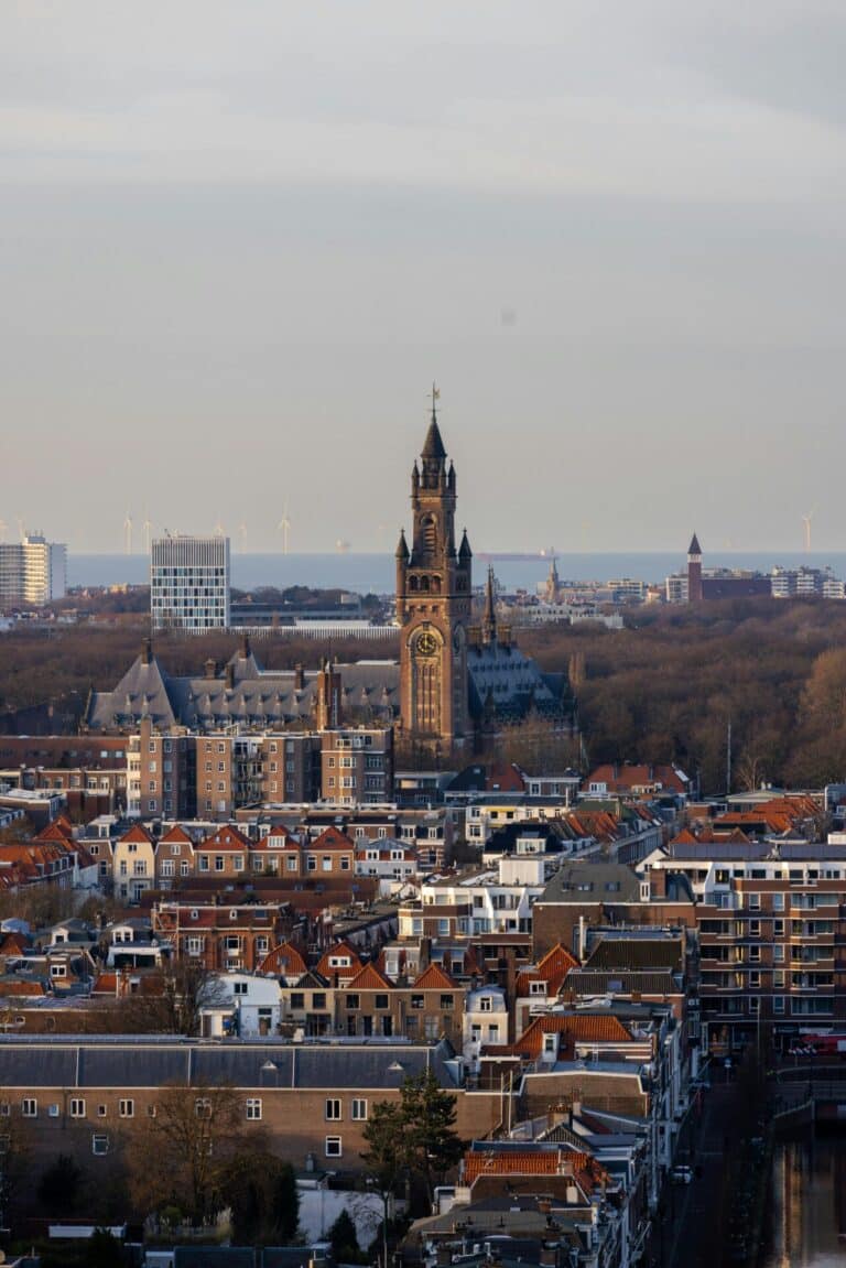 An elevated view over The Hague, showing the Peace Palace rising above the city with the North Sea beyond.