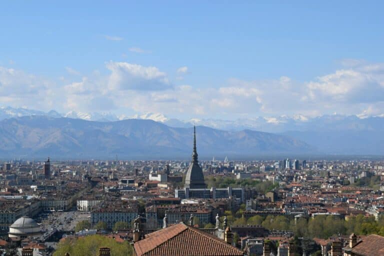 An elevated view of the Turin cityscape featuring the Mole Antonelliana with the snow-capped Alps in the background.