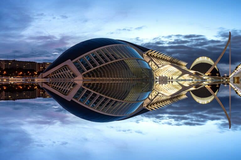 The illuminated City of Arts and Sciences complex in Valencia is perfectly reflected in the calm water at dusk.