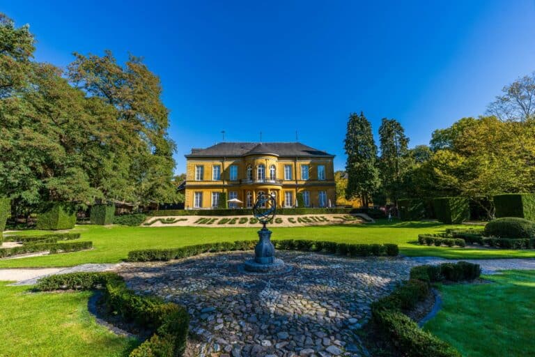 The yellow manor of Kasteel Schaloen seen from its formal gardens on a sunny day in Valkenburg.