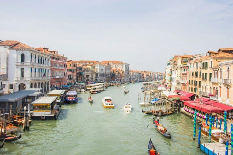 A daytime view of the bustling Grand Canal in Venice, with many gondolas and boats on the water.