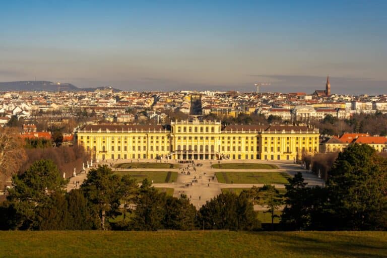 An elevated view of the historic Schönbrunn Palace and its gardens with the Vienna cityscape in the background.