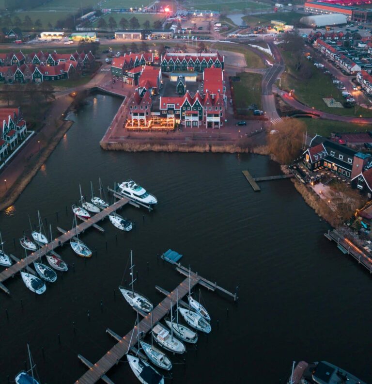 An aerial view of the Volendam harbor and village at dusk, with many boats docked in the marina.