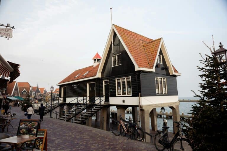A traditional black wooden building with a red tile roof stands on stilts over the water in Volendam.