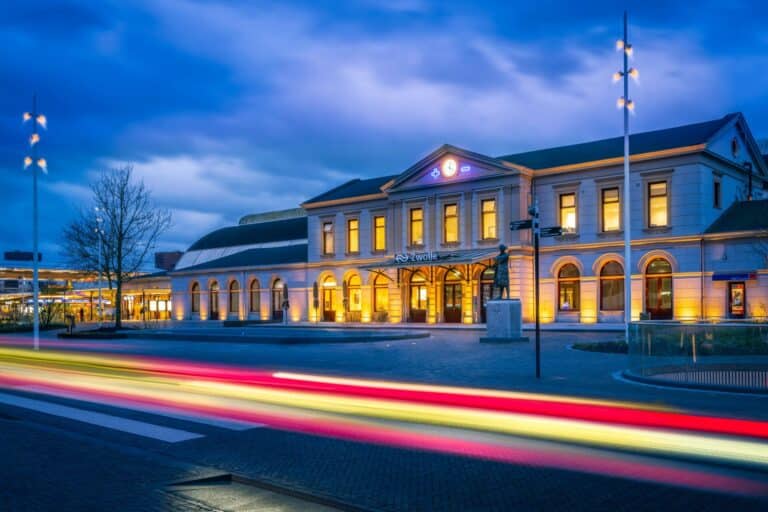 The historic main train station in Zwolle is illuminated at dusk with long light trails from traffic.