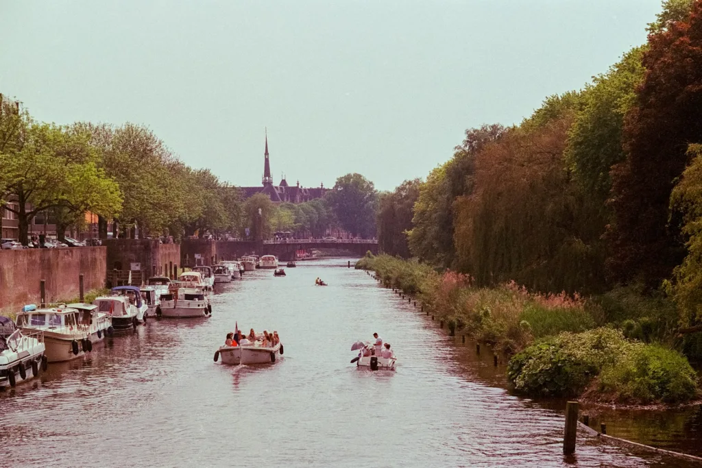 City Game Den Bosch boats gliding through serene waters, surrounded by lush greenery and historic architecture in the distance
