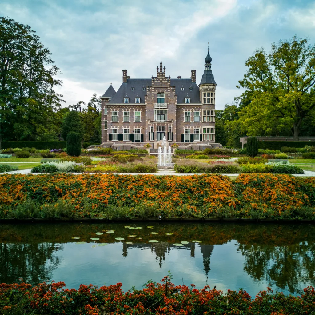 City Game Eindhoven stunning view of the Kasteel Geldrop in Eindhoven, surrounded by vibrant gardens, a serene pond with lily pads, and a central fountain, exuding timeless elegance and charm.