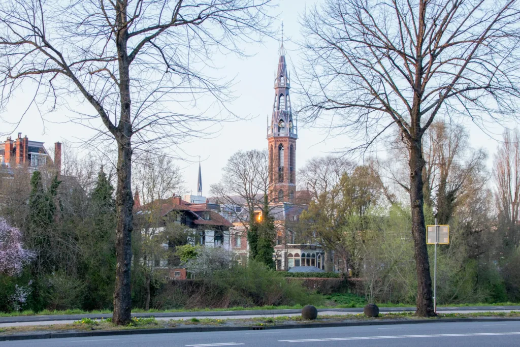City Game  Groningen"scenic view of a historic church tower rising above lush greenery and charming buildings, framed by bare trees on a quiet street.